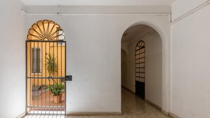 Un couloir doté d’un sol carrelé, d’une grille en métal ornée d’un motif en forme de soleil, et d’une plante en pot.