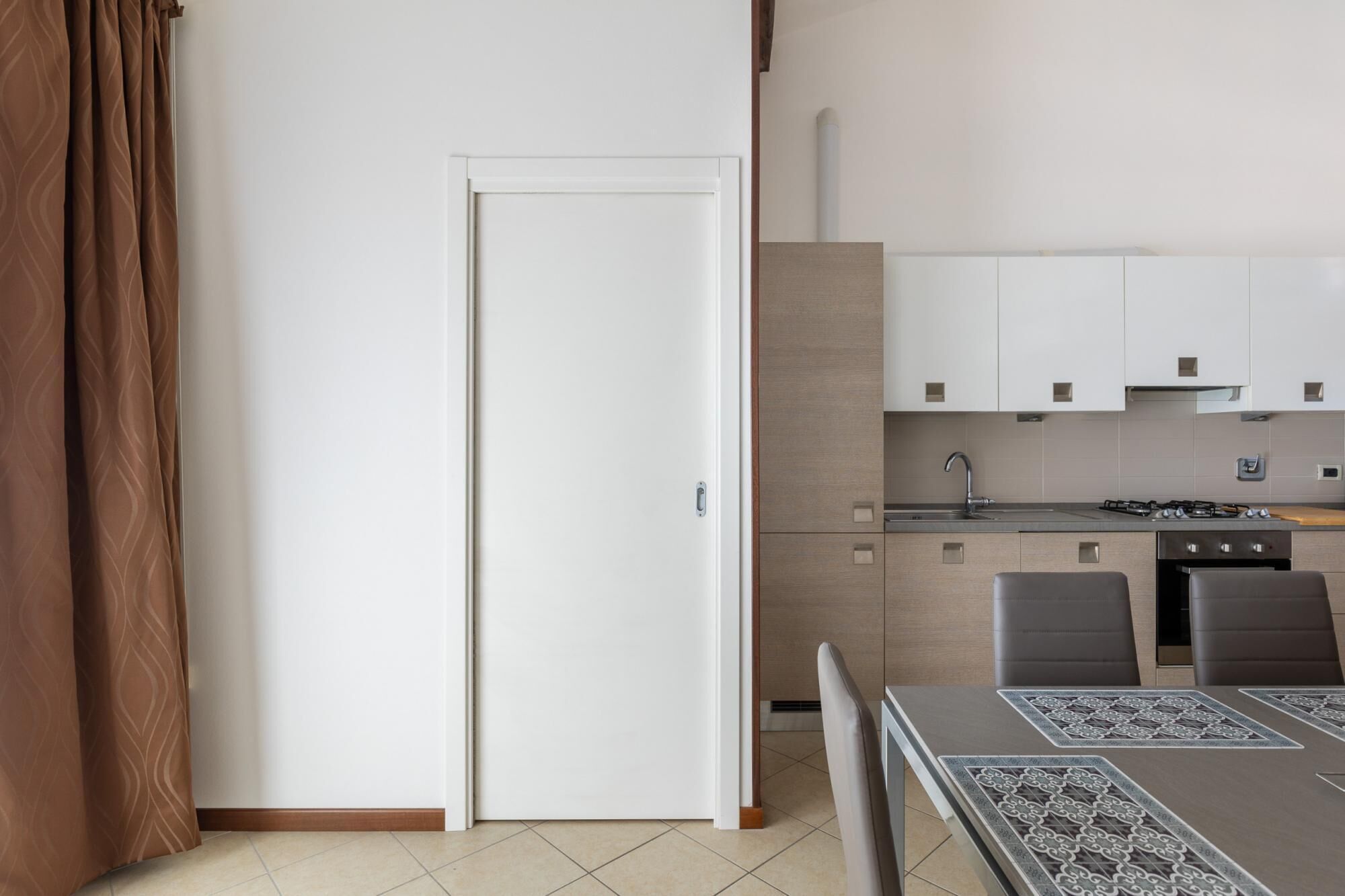 Une cuisine moderne avec des meubles blancs, une cuisinière à gaz et un évier. On y trouve une table à manger avec des chaises et un chemin de table à motifs.