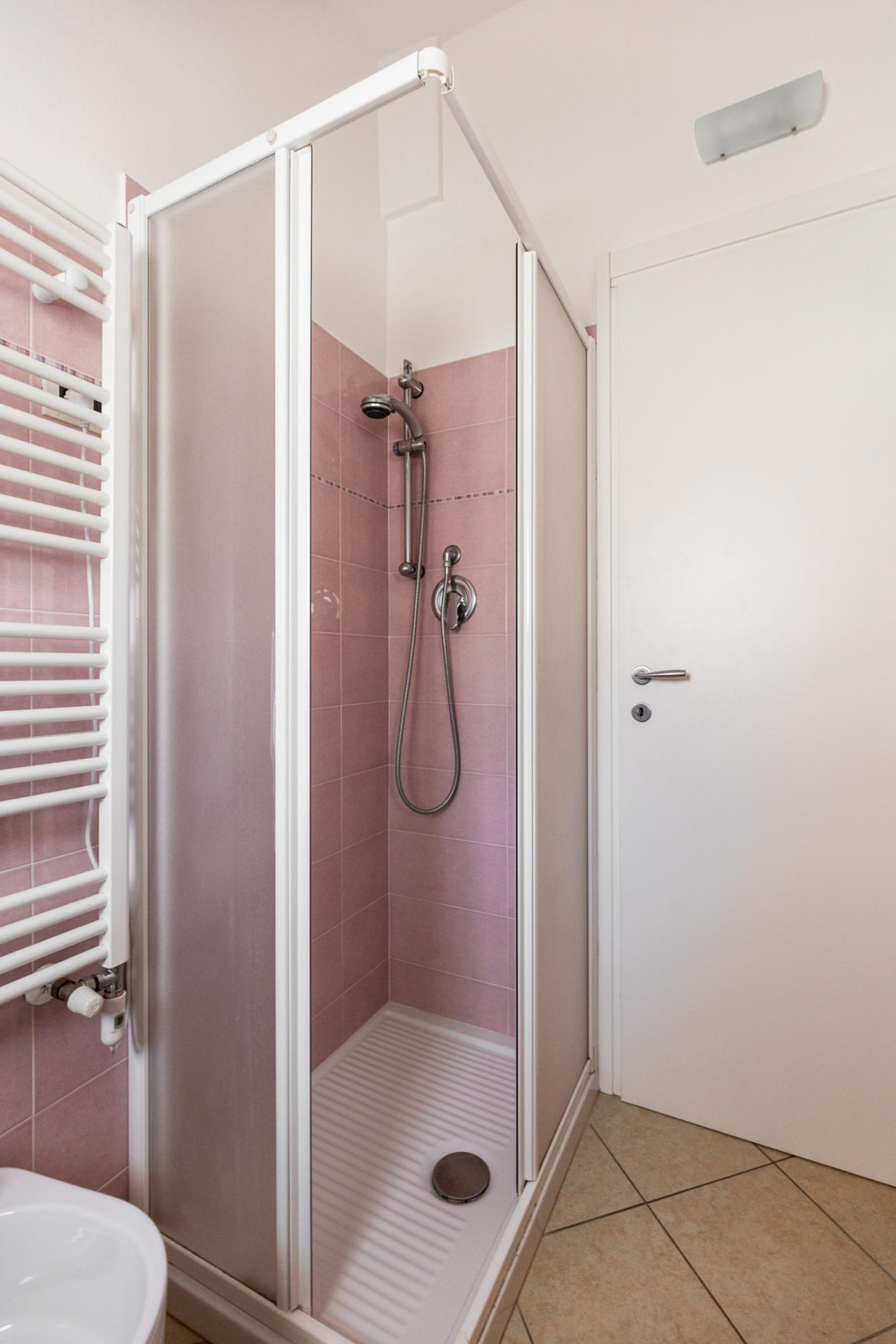 A shower area with a glass door, pink tiles, and a white sink.