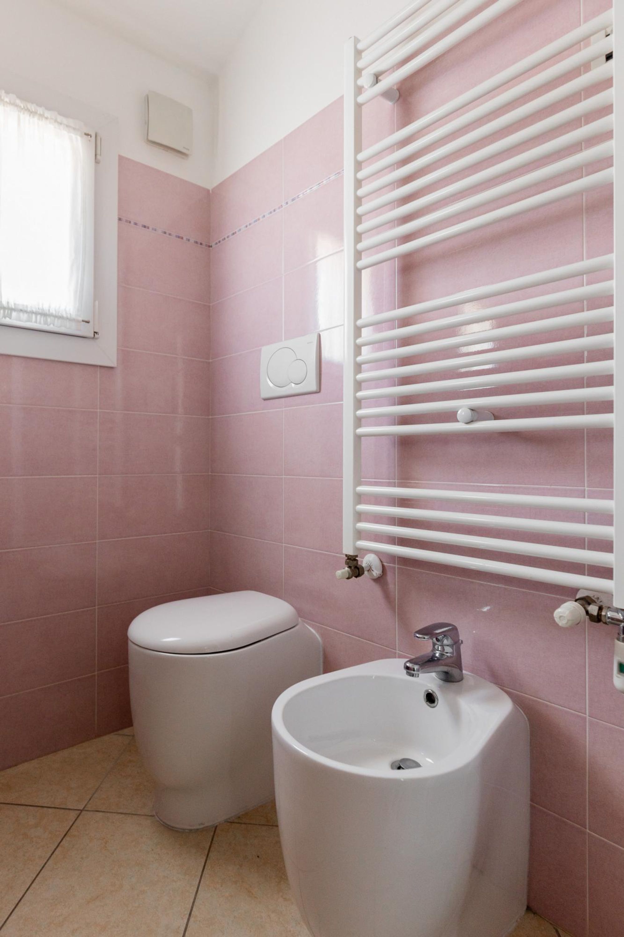 A bathroom with pink tiles, a toilet, a bidet, and a white towel rack.