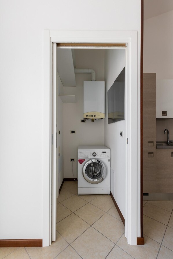 Une buanderie équipée d’un lave-linge et d’un sèche-linge, un petit coin cuisine avec un évier et un sol carrelé.
