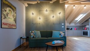 Een moderne woonkamer met een groene bank, een klein bijzettafeltje met een boek en een kopje, en een wandlamp.