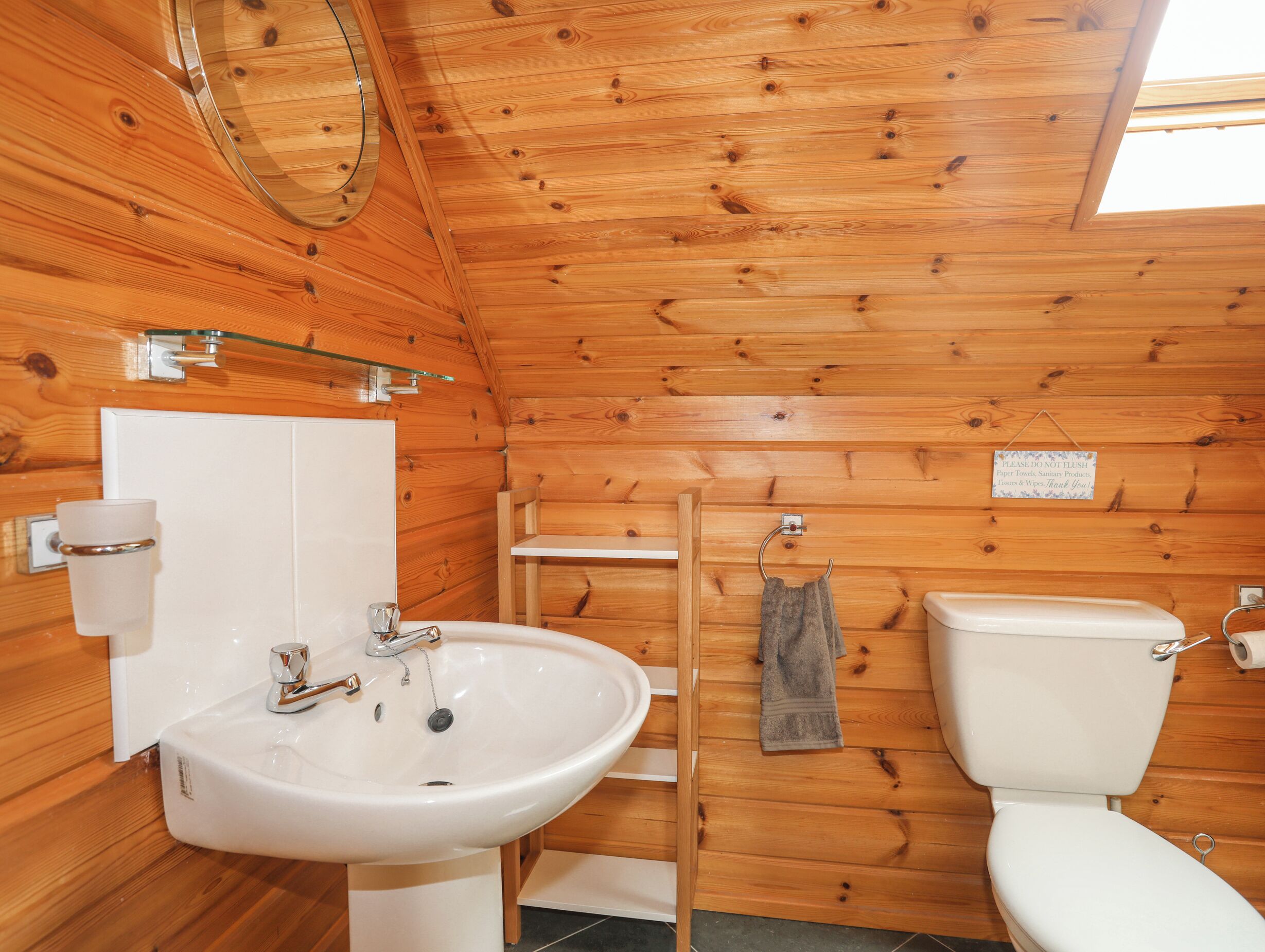 Un baño de cabaña de madera con lavamanos blanco, inodoro y mampara de vidrio.