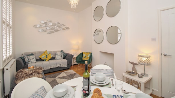 Zona pranzo con tavolo apparecchiato per due, un lampadario e un divano con cuscini.