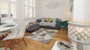 Un soggiorno moderno con zona pranzo, un divano grigio con cuscini decorati, un tappeto geometrico e una lampada ornamentale.