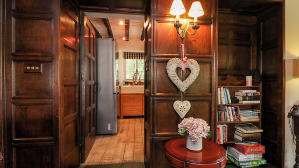 Een houten interieur met een boekenplank, een kleine tafel met een bloevas, en een hartvormige decoratie aan de muur.
