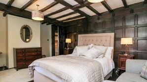 Een slaapkamer met een groot bed, houten hoofdbord, twee nachtkastjes met lampen, een dressoir en een spiegel aan de muur.