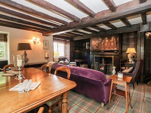 Ein traditionell eingerichteter Raum mit Holztisch, Stühlen, einem violetten Sofa, einem Kamin und einer Holzbalkendecke.