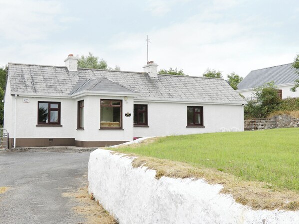 A white cottage with a grey roof, a chimney, and a small porch. - Daffodil Cottage (Grange)