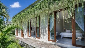 A bungalow with a wooden deck, a bedroom with a bed and curtains, and hanging vines. - Luxury Spacious Family 5BR Villa Big Pool & Garden (Canggu)