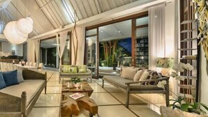 A spacious living area with a high ceiling, large windows, and a variety of seating arrangements. - Luxury Spacious Family 5BR Villa Big Pool & Garden (Canggu)