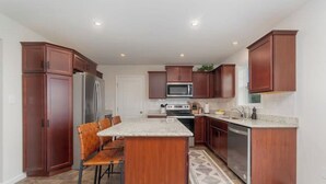 A kitchen with wooden cabinets, a stainless steel refrigerator, a microwave, and a built-in oven. There is a dining area with a wooden table and chairs.
