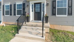 A two-story house with a front porch, a black front door, and a set of concrete steps leading to the entrance.