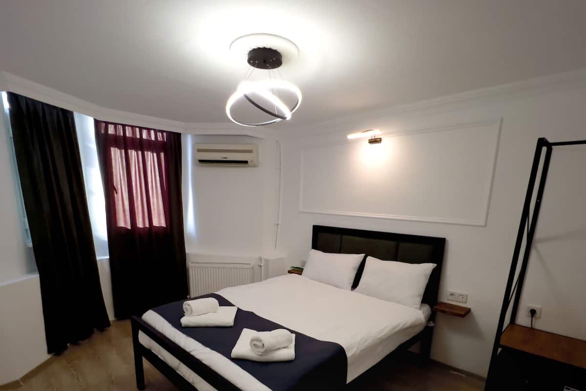 A neatly made bed with white linens, a bedside table with a lamp, and a large mirror on the wall.