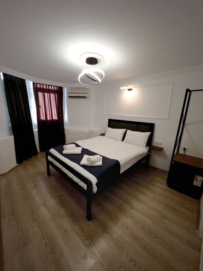 A neatly made bed with white linens, a bedside table with a lamp, and a large mirror on the wall.