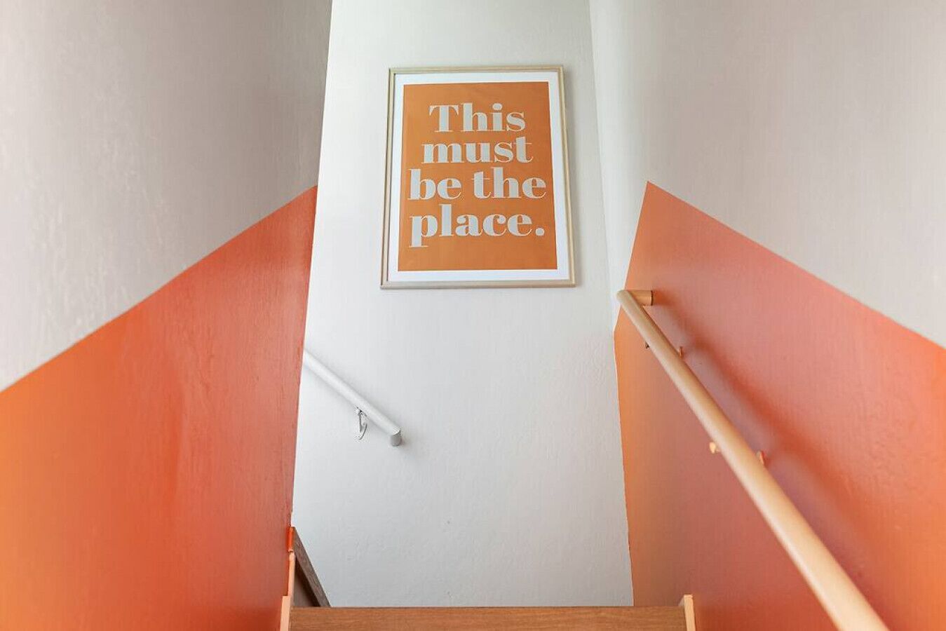 A staircase with orange walls and a framed sign that reads "This must be the place."