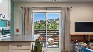 Une cuisine moderne dotée d’un grand îlot central, d’un coin repas avec des chaises, d’un téléviseur et d’une vue sur un paysage montagneux, visible à travers une porte-fenêtre coulissante.