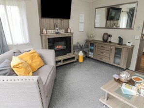 A living room with a sofa, a fireplace, a television, a cabinet, and a coffee table with books and a teapot. - Mulberry Lodge (Morpeth)