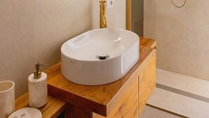 A modern bathroom with a round mirror, a white sink, and a gold showerhead. - Repetita Juvant (Rome)