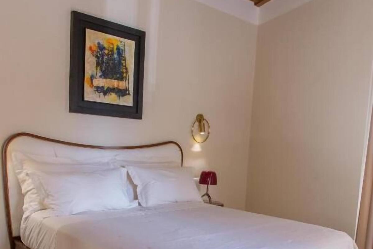 A bedroom with a wooden bed, a framed painting on the wall, and a bedside lamp.
