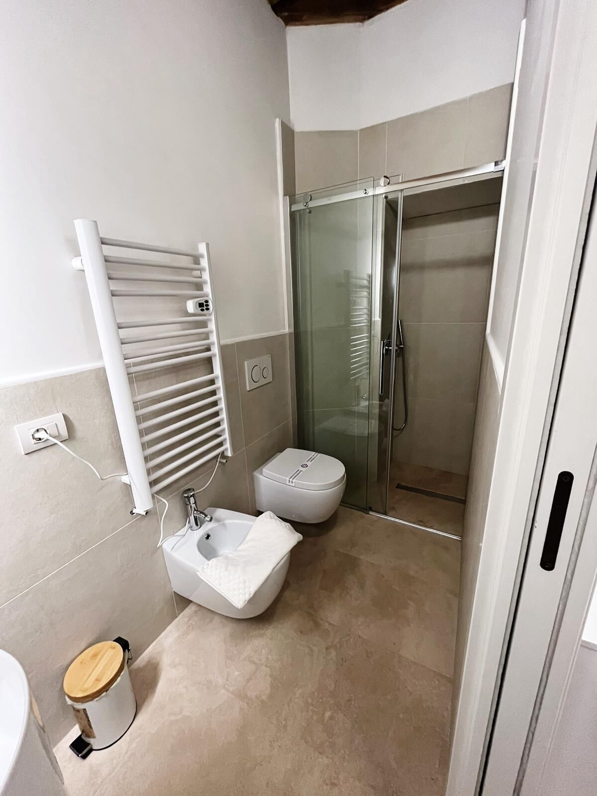 Een moderne badkamer met een douchecabine van glas, toilet, wastafel en een handdoekrek.