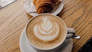 A table with a cup of coffee and a croissant on a wooden table. - Repetita Juvant (Rome)