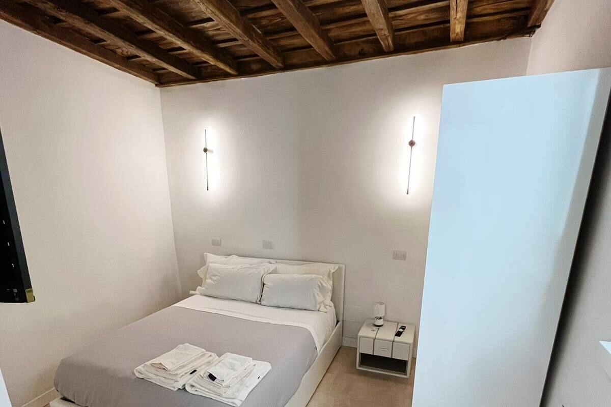 A bedroom with a wooden ceiling, a bed with white bedding, two bedside tables, and a nightstand.