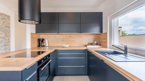 A modern kitchen with dark cabinets, a wooden countertop, a built-in oven, and a large window providing natural light. - Villa Dvor (Vodnjan)