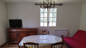 Een eethoek met een ronde tafel, stoelen, een televisie op een kast, een raam en een rode bank.