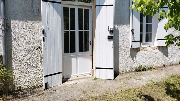 Een wit gebouw met een brede open deur en een raam met luiken.