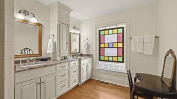 A bathroom with a large mirror, two sinks, a vanity, and a window with a stained glass design.