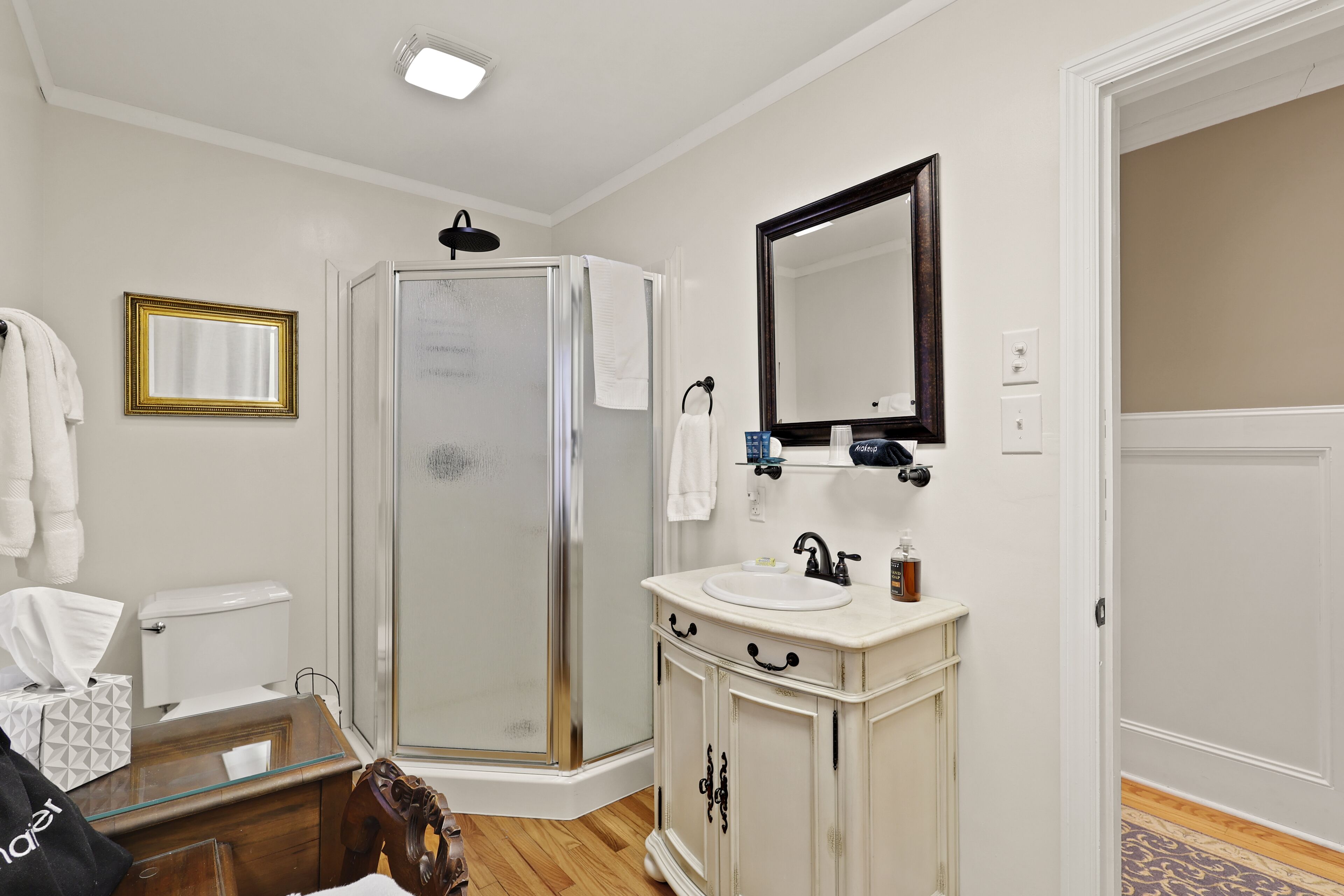 Une salle de bain avec une douche à parois de verre, un lavabo blanc avec un miroir au-dessus et un meuble-lavabo en bois.