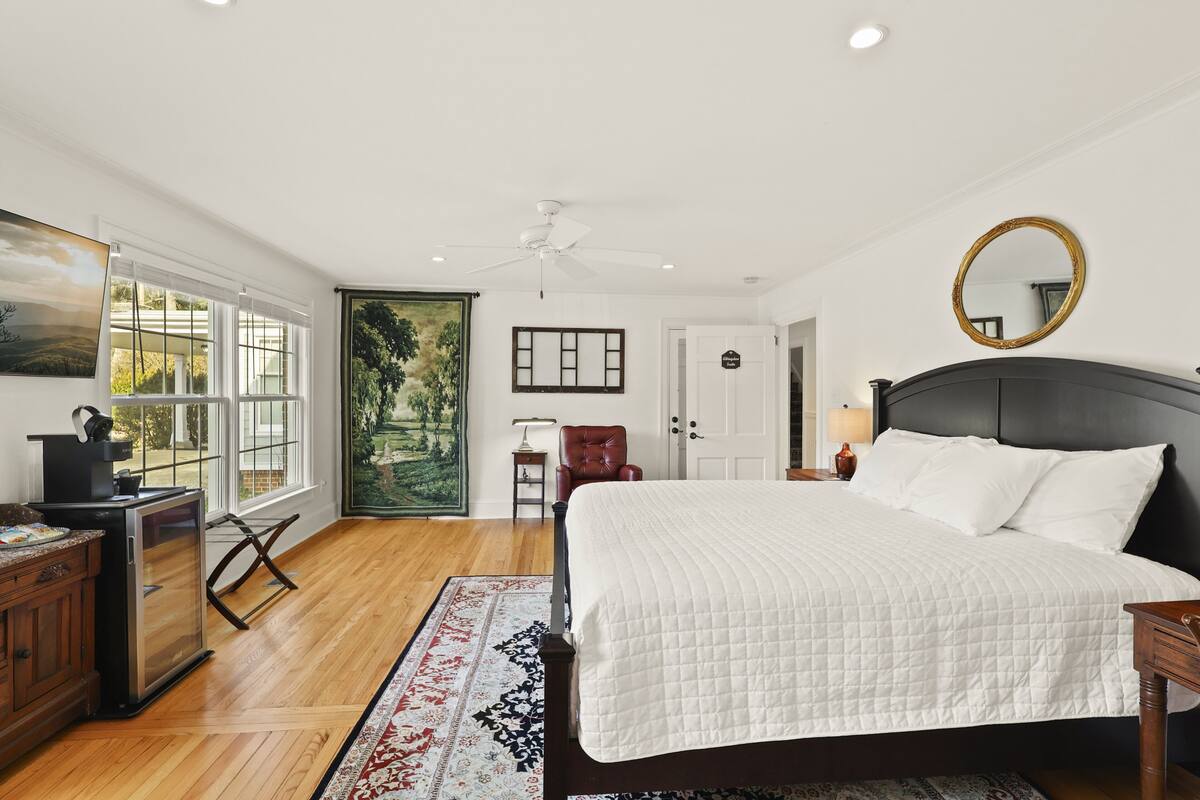 A bedroom with a bed, a desk, a chair, a ceiling fan, a window, and a door.