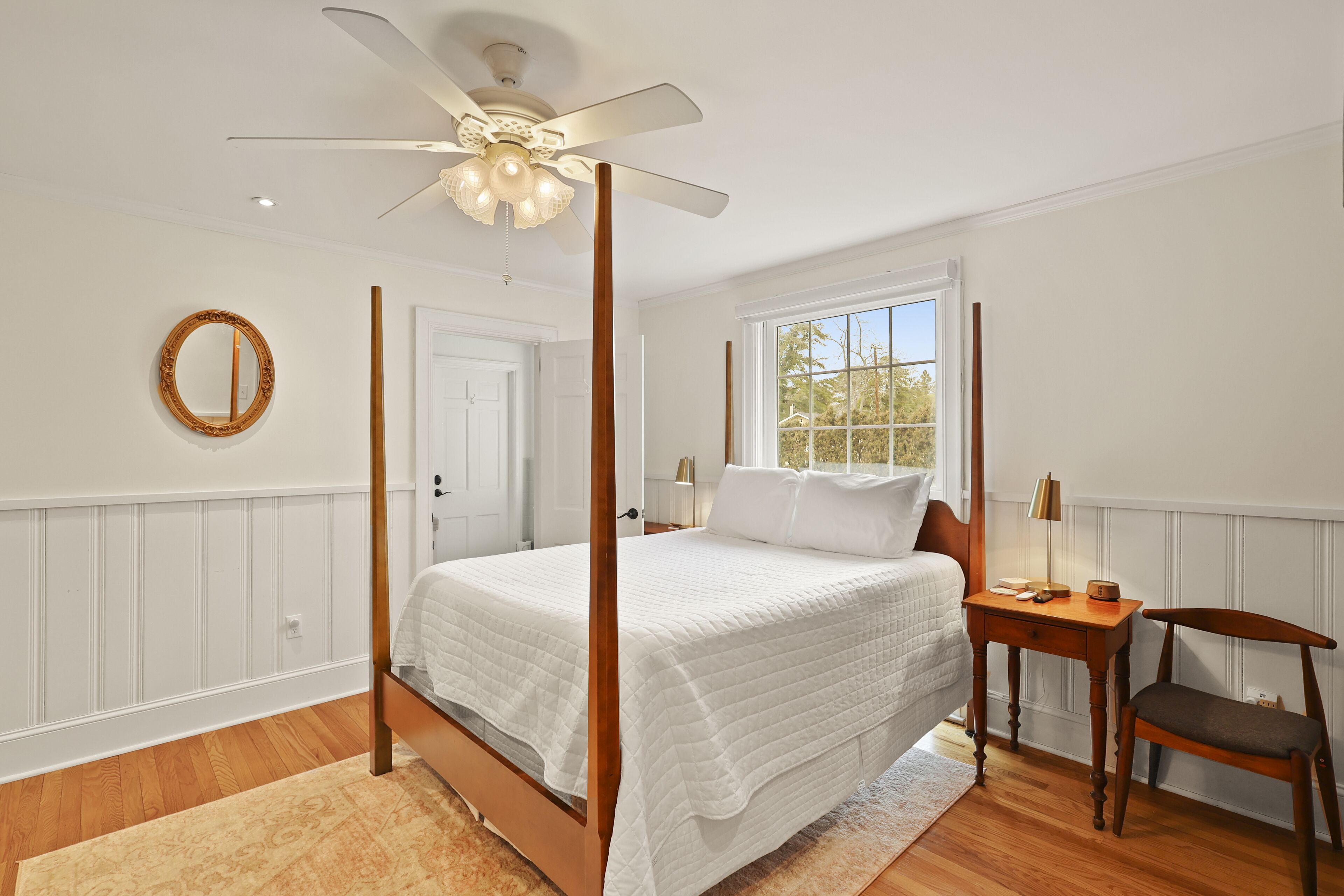 A four-poster bed with a wooden frame, a bedside table with a lamp, and a chair.