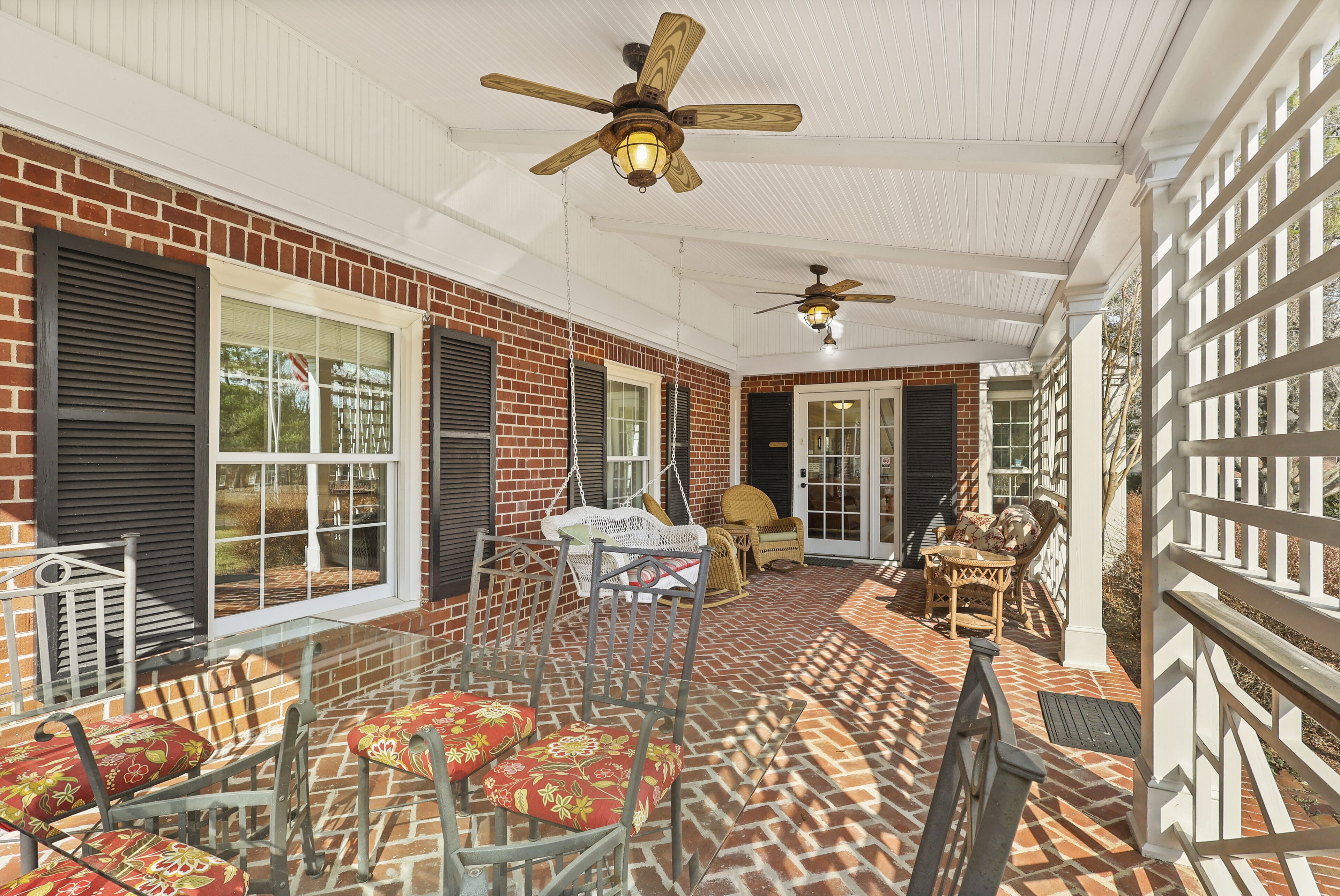 Ein überdachter Patio-Bereich mit Backsteinwänden, zwei Deckenventilatoren und Gartenmöbeln, darunter Stühle und ein Tisch.