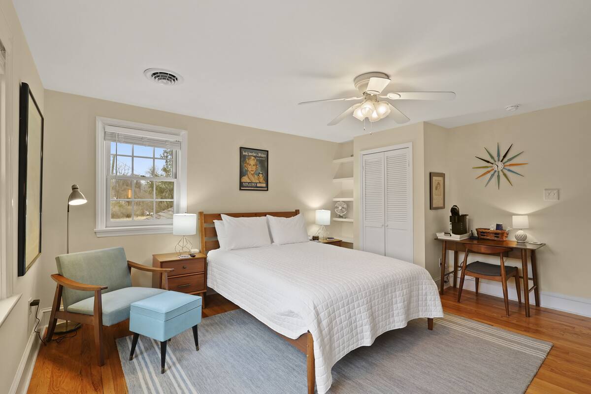 A bedroom with a bed, nightstands, a chair, a desk, a ceiling fan, and a window.
