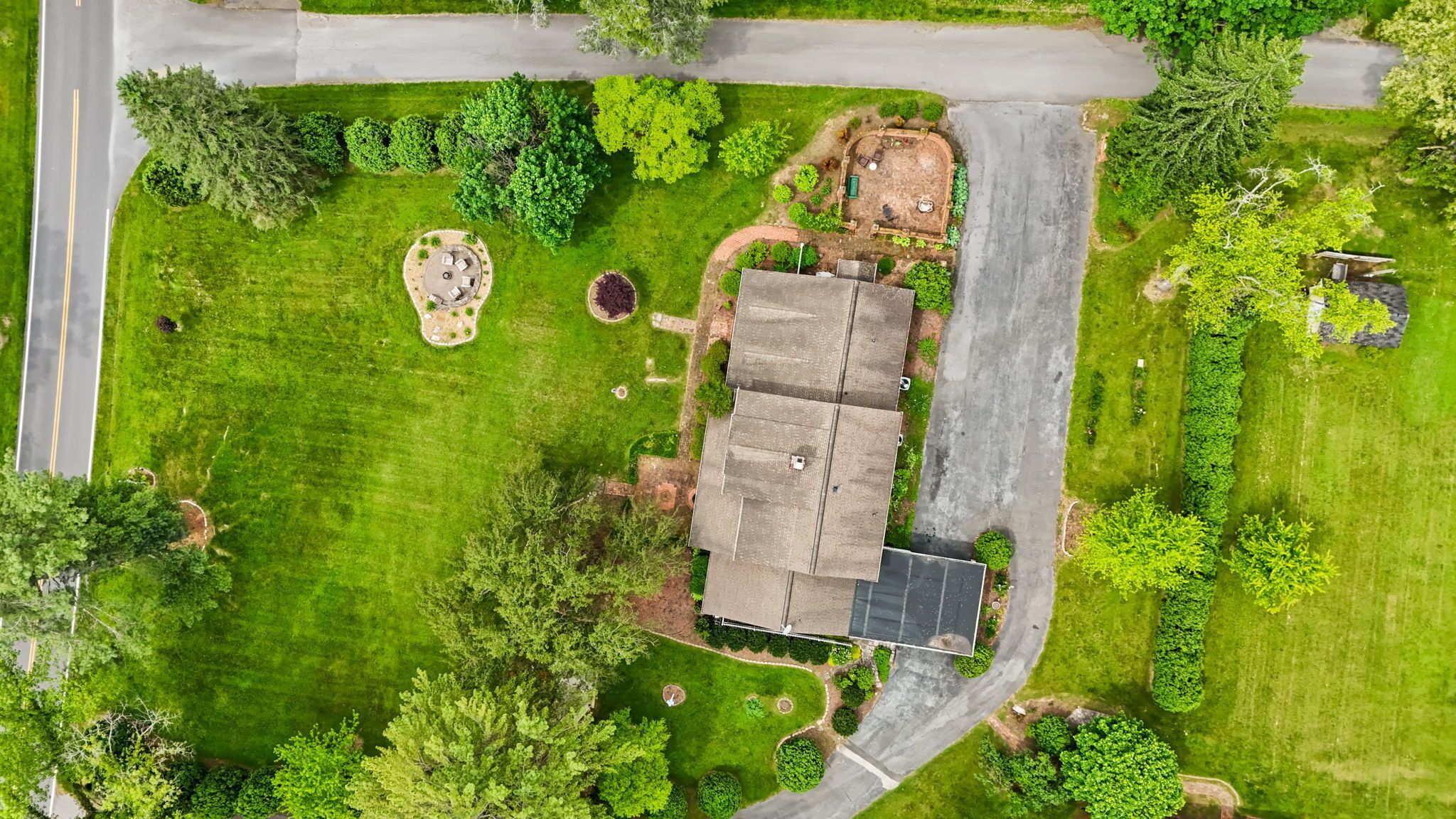 An aerial view of a residential property with a large house, a driveway, and a well-maintained lawn.