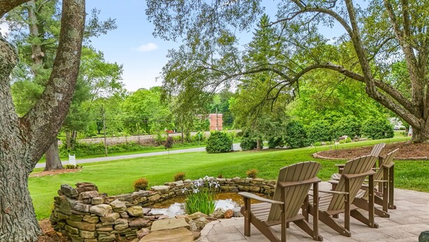 Eine Terrasse mit Adirondack-Stühlen, einem Steinteich und einem gepflegten Rasen.