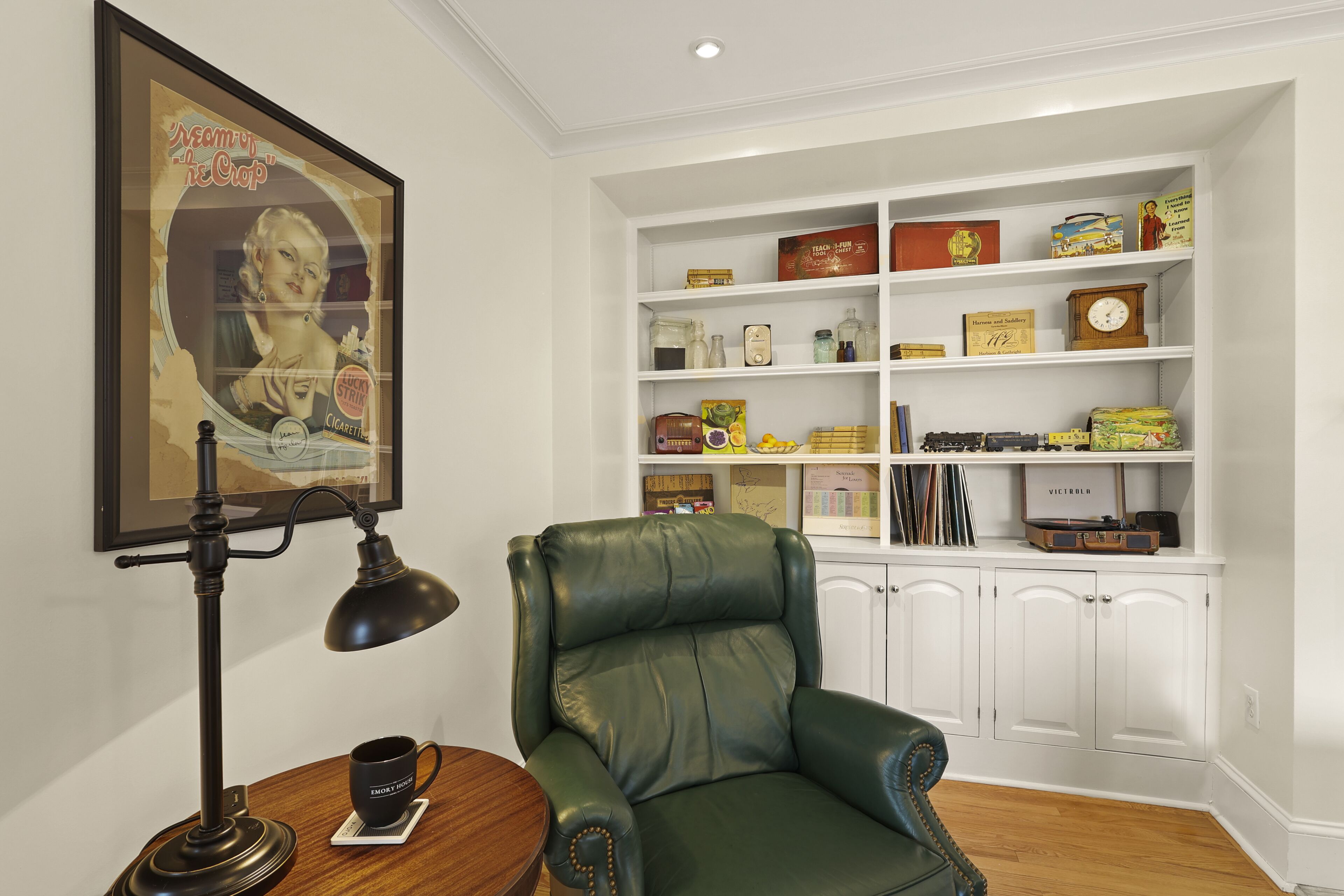 Une pièce comprenant un fauteuil en cuir vert, un bureau avec une lampe et une bibliothèque remplie de divers objets.