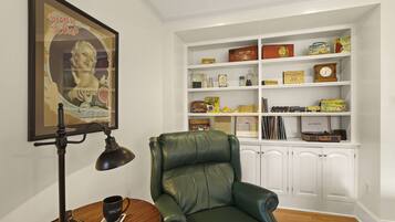 Une pièce comprenant un fauteuil en cuir vert, un bureau avec une lampe et une bibliothèque remplie de divers objets.
