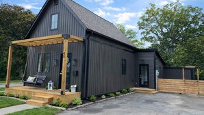 Un bâtiment moderne à deux étages, doté d’une façade sombre, d’un porche en bois et d’un petit jardin.