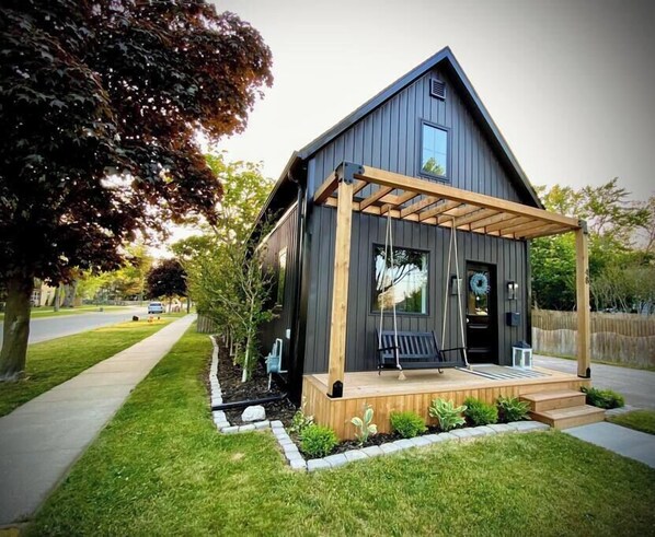A modern house with a wooden porch, a small garden, and a clear sky. - Stylish Getaway - Walk to downtown + Parks, Fenced yard + Firepit + Smart TVs (Kingsville)