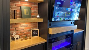 Un salon moderne avec un mur en briques, des étagères en bois, un téléviseur et un panneau décoratif représentant un ange.