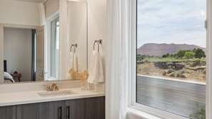 Ein Badezimmer mit einem großen Spiegel, einem Waschbecken und einem Fenster mit Blick auf eine Straße und Berge.