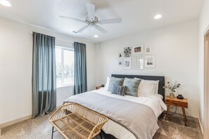 Una camera da letto con un letto, una ventola a soffitto, una finestra con tende, un comodino con una lampada e decorazioni alle pareti.