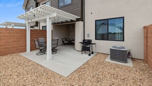 Ein überdachter Patio-Bereich mit Gartenmöbeln, einem Grill und einer Klimaanlage.