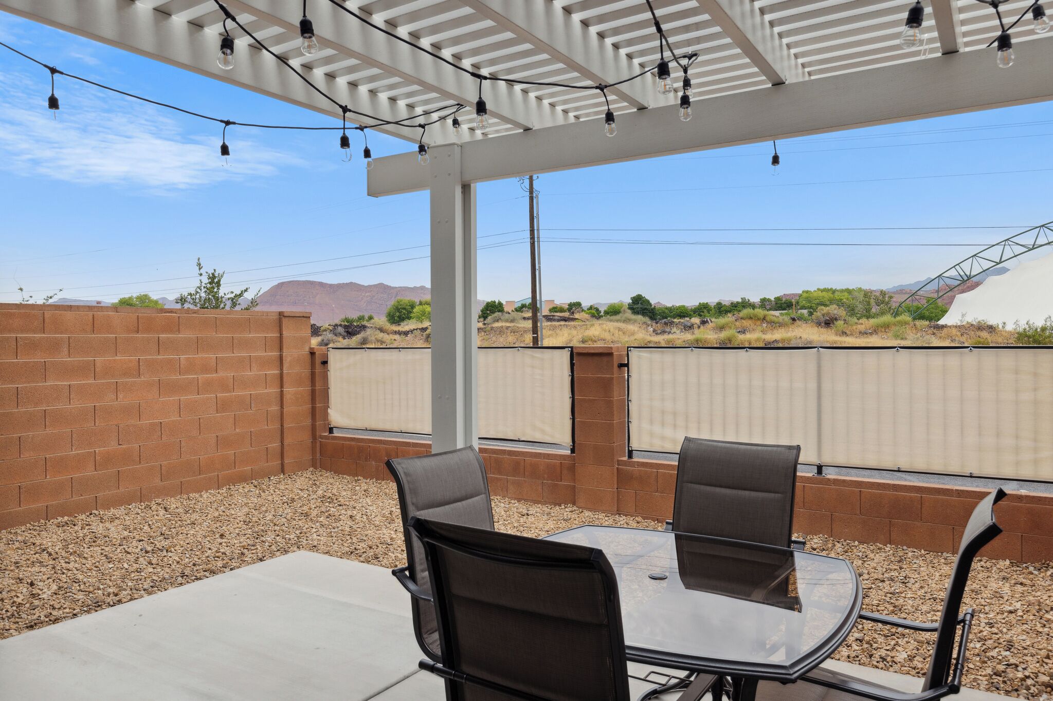An outdoor patio with a table and chairs, a pergola with string lights, and a view of the desert landscape.