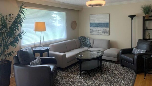 A living room with a sectional sofa, a glass coffee table, a floor lamp, and a potted plant. - Centrally located one bedroom + Office (Calgary)