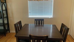 A dining area with a rectangular table, four chairs, a chandelier, and a window with blinds. - Centrally located one bedroom + Office (Calgary)