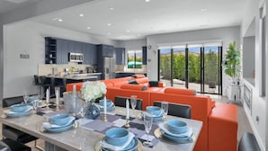 A modern kitchen with dark cabinets, a dining area with orange seating, and a view of the outdoors. - New+Modern/Pool/Spa/Gameroom/Poker/Massage chair (Indio)